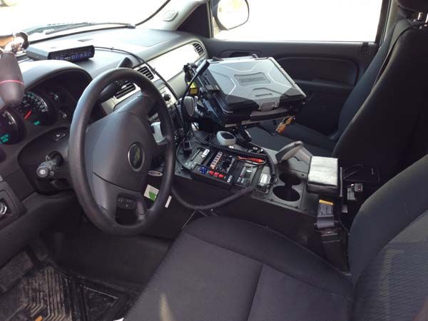 Interior of a police vehicle with steering wheel, computer, console, and black seats.