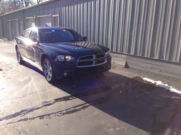 Black Dodge Charger police car parked next to a corrugated metal building, sunlight casting shadows.