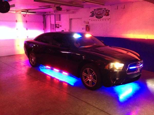 Black car with blue and red underglow and flashing lights inside a garage.