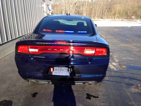 Rear view of a dark blue Dodge Charger police car with flashing red and blue lights, parked outdoors.