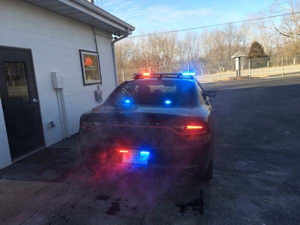 Police car with flashing blue and red lights parked outside a building, with visible exhaust.