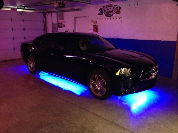 Black Dodge Charger with blue underglow lights in a garage.
