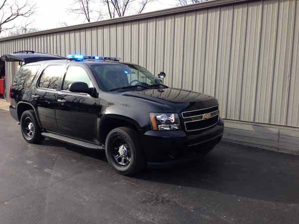 Black police SUV with blue lights parked outside a building.