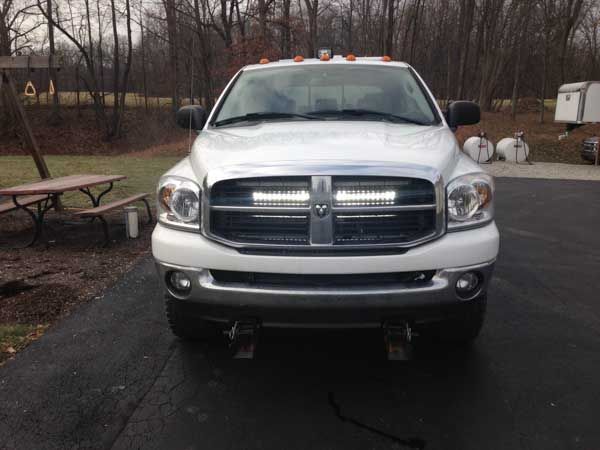 White Dodge Ram truck with LED light bars in the grill, parked outside on a paved surface.