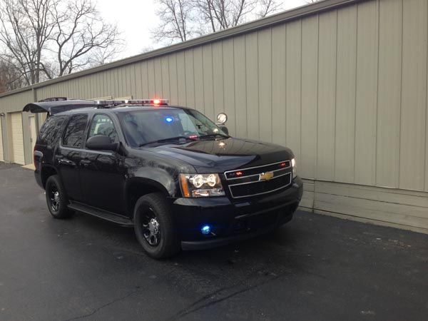Black police SUV with flashing blue and red lights parked near a building.