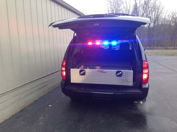 Black SUV with open trunk, flashing red and blue lights, and a metal toolbox inside.