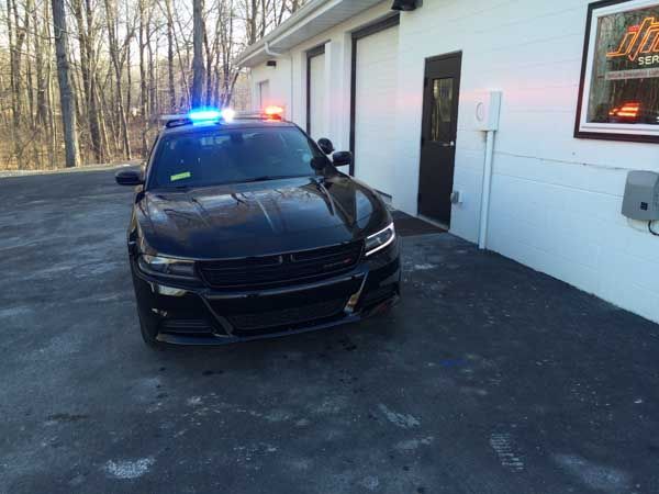 Black police car with flashing blue and red lights parked outside a white building.