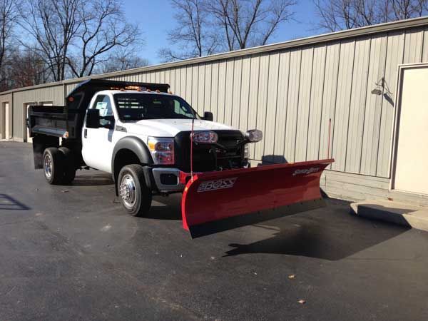 White Ford dump truck with a red snowplow parked in front of a building.