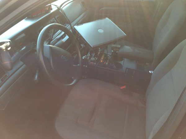 Interior of a police car with a laptop mounted on the console between the seats. Gray seats, steering wheel, and console.