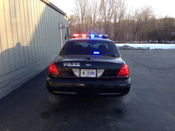 Rear view of a black police car with flashing red and blue lights; parked outside a building.