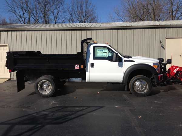 White Ford dump truck with a snowplow parked in front of a building.