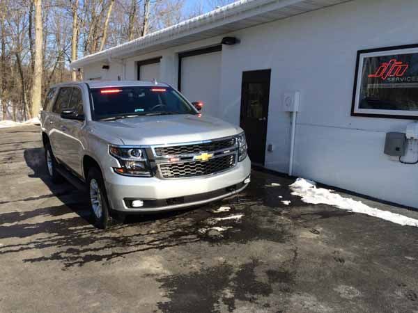 Silver SUV with red emergency lights parked in front of a white building with a garage door.