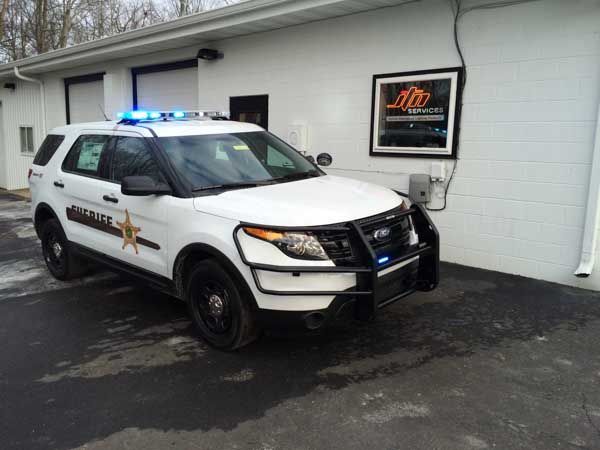 White Sheriff's SUV with blue lights parked outside a building, with a protective grill on the front.