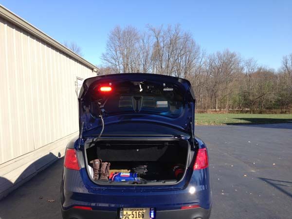 Blue car trunk open, with red light bar, parked outdoors.