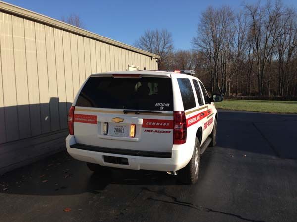 White Chevy Tahoe fire vehicle parked next to a tan building with red and gold striping.