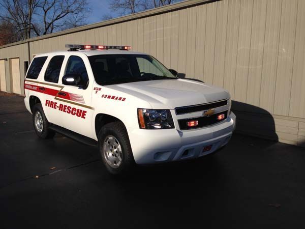 White fire rescue SUV with red stripes and lights parked near a building.