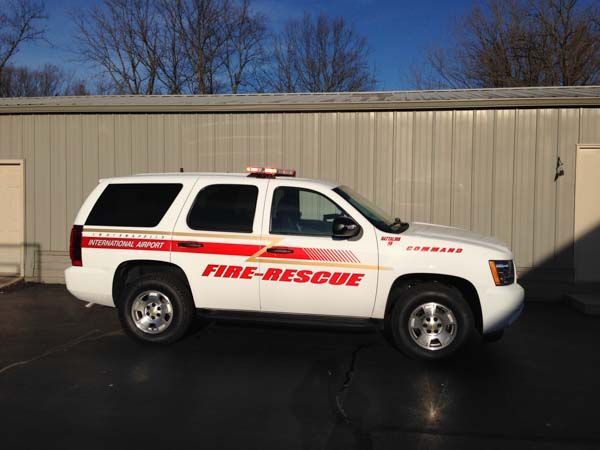 White fire-rescue SUV parked in front of a building with overhead emergency lights.