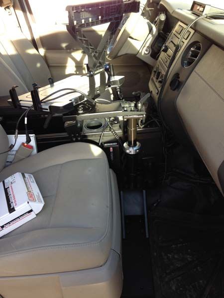 Interior of a vehicle with specialized equipment mounted between seats; beige seat, black dashboard.