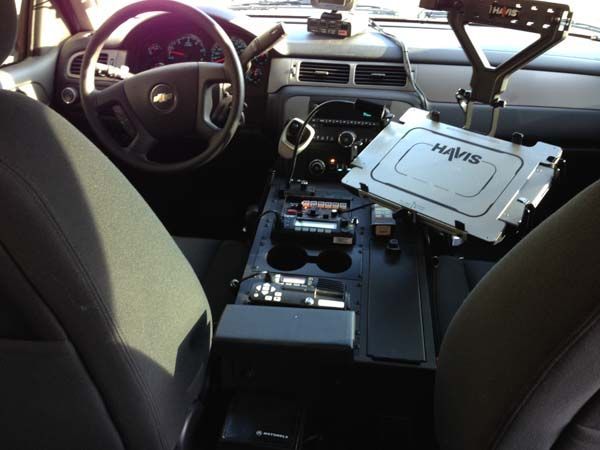 Interior of a police vehicle, with a central console containing radio and computer, and a mounted tablet.