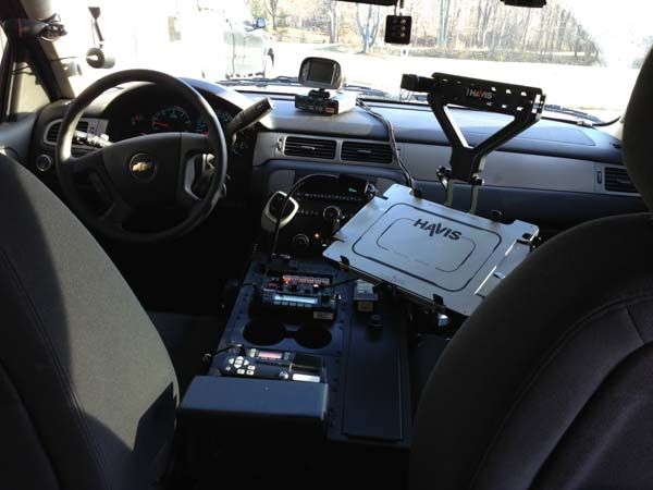 Interior of a police vehicle with mounted computer and equipment. Black and gray. Dashboard visible, with steering wheel.