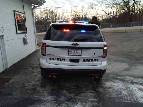 White sheriff's SUV with flashing red and blue lights, parked near a building.