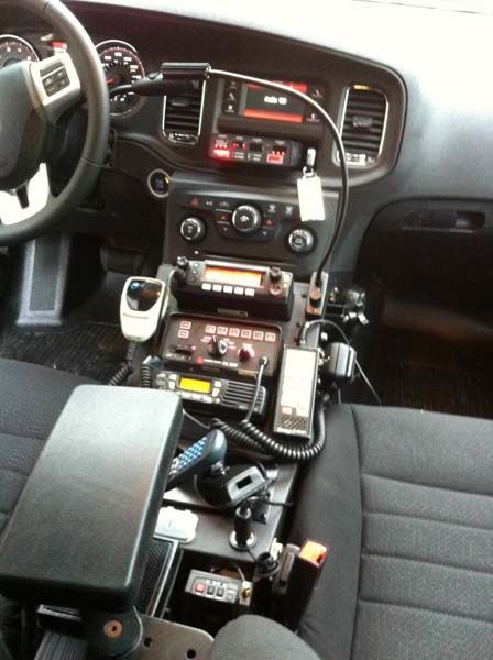 Interior of a police car with radio equipment mounted on the console and dashboard. Black and gray colors dominate.