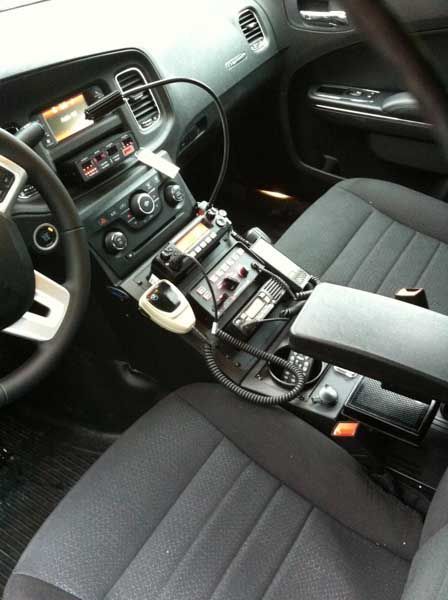 Interior of a police car, dashboard with radio equipment, center console, and black seats.