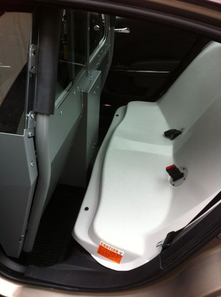 Interior of police car back seat, showing a prisoner partition and white molded seat.