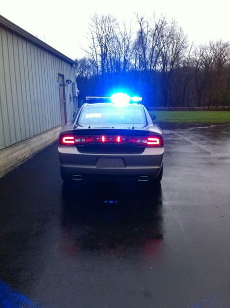 Police car with flashing blue and red lights, parked near a building on a wet pavement.