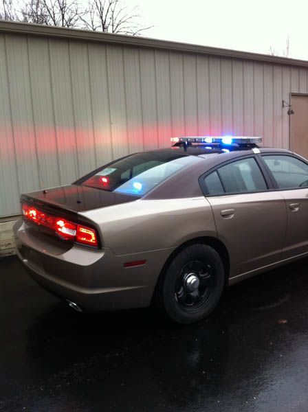 Brown police car with flashing blue and red lights against a tan building.