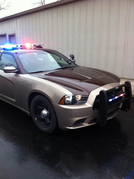Police car, two-tone tan and brown, with flashing blue and red lights on, parked in front of a building.