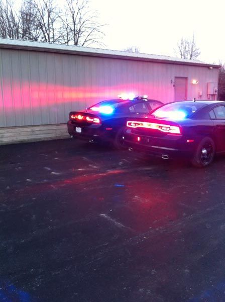 Two black police cars with flashing red and blue lights parked outside a building at night.