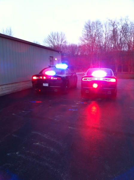 Two black police cars with flashing red and blue lights are parked outside a building.