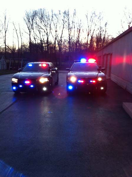 Two police cars with flashing red and blue lights illuminated, parked outdoors at dusk.