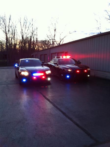 Two police cars with flashing red and blue lights parked outside a building at dusk.