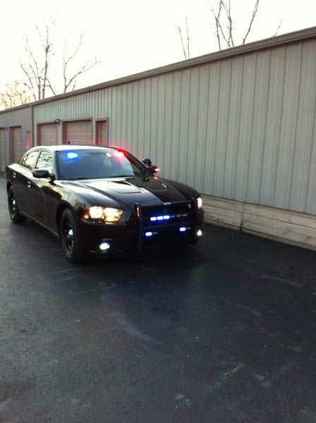 Black police Dodge Charger with flashing red and blue lights, parked near a building.