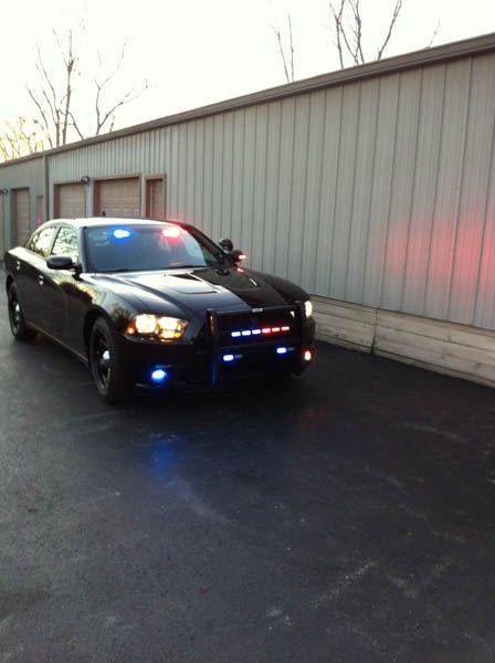 Black police Dodge Charger with flashing red and blue lights, parked next to a building.