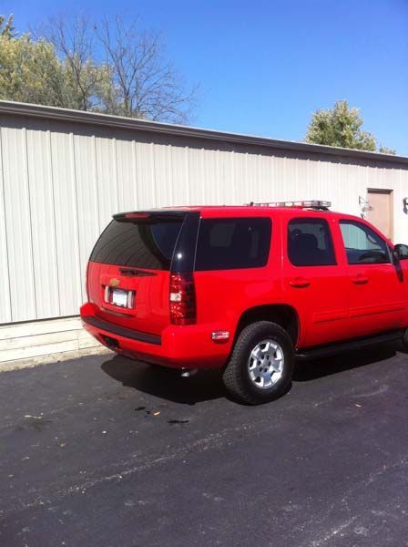 Red SUV parked next to a gray building on a sunny day.