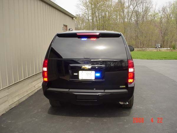 Black Chevrolet SUV with emergency lights on; parked outside building.