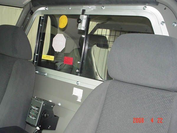 Interior of a vehicle, possibly a police car. Shows rear seats with a protective barrier and window.
