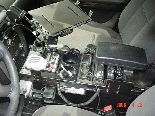 Police car interior showing mounted equipment: radio, computer, cup holders, console.