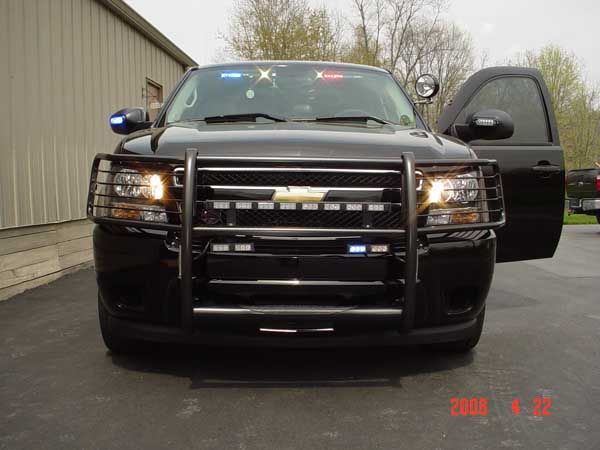 Black police SUV with emergency lights, push bar, and open driver-side door, parked in front of a building.