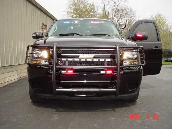 Black police SUV with emergency lights, grill guard, and open door.