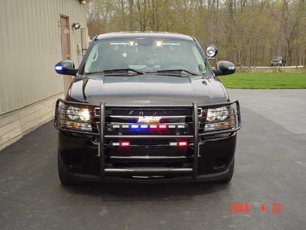 Black police SUV with emergency lights and push bar in front of building.