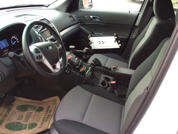 Interior view of a police car with center console equipment, computer mount, and driver's seat.