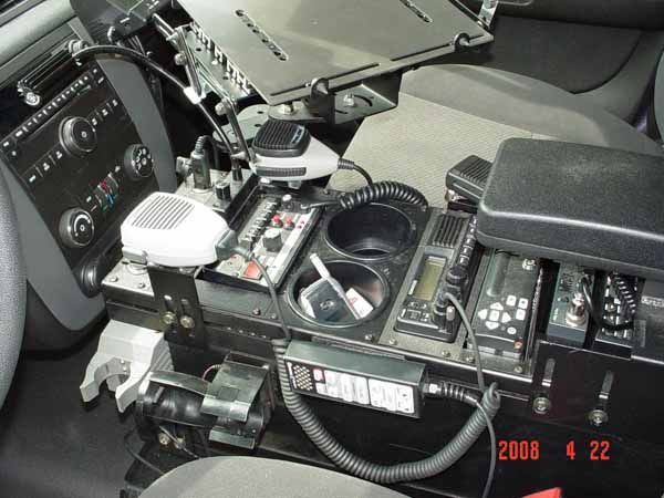 Police car center console with mounted equipment including radios, microphones, and cup holders.