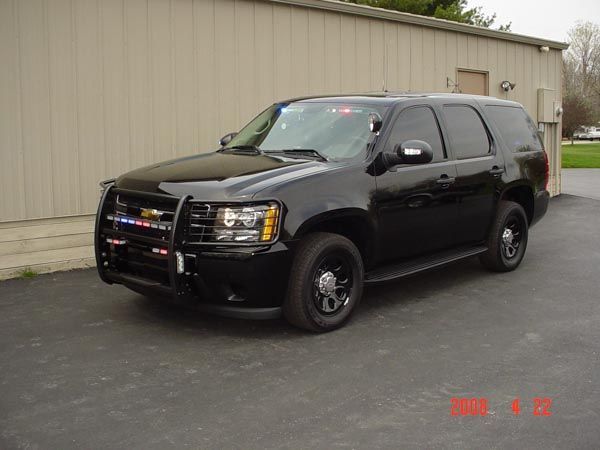 Black police SUV parked in front of a tan building; emergency lights and front push bar visible.