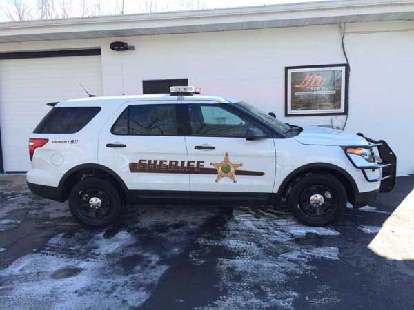 White Sheriff SUV parked in front of a white building with black tires and the word 