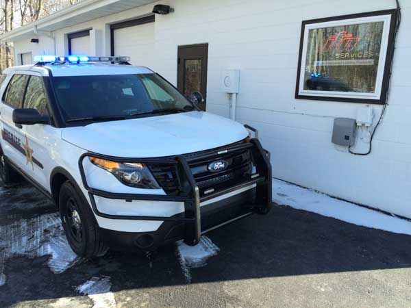 White police SUV with blue lights parked outside a building, snowy ground.