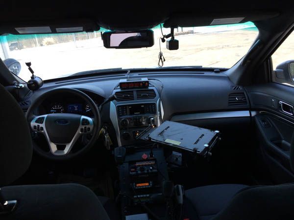 Interior view of a police car, dashboard visible with equipment, windshield, and steering wheel.